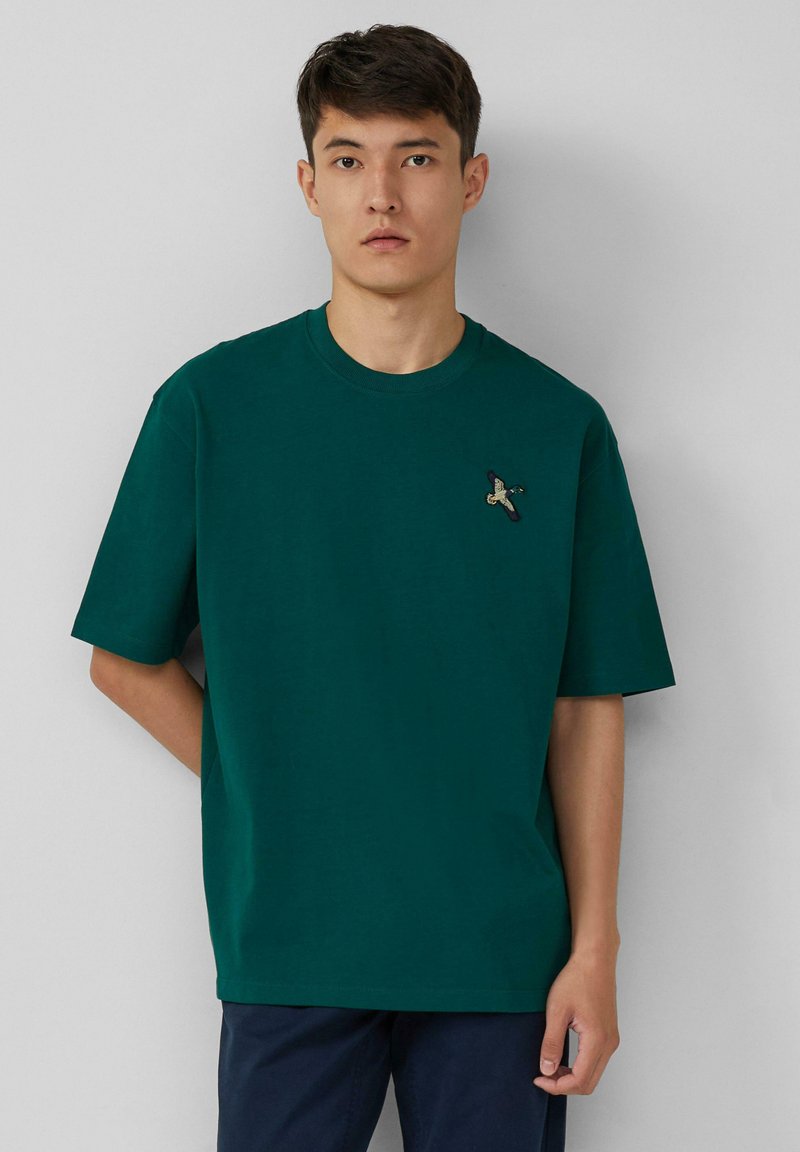 Groen katoenen t-shirt met een ronde hals, korte mouwen en een klein geborduurd ontwerp nabij de borst. Eenvoudig en casual ontwerp.