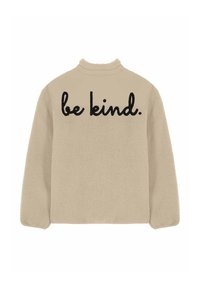 Veste en polaire beige à manches longues avec un texte noir en cursive "be kind." sur le haut du dos.