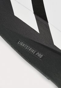 Cinghia di sandalo Adidas in bianco e nero con etichetta "LIGHTSTRIKE PRO" visibile sulla superficie del suola testurizzata.