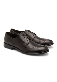 Brązowe skórzane buty wizytowe z detalami w stylu brogue, wyróżniające się gładkim wykończeniem, okrągłym noskiem i sznurówkami. Płaska podeszwa z subtelnymi akcentami przeszycia.