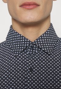 Marineblauw overhemd met een patroon in wit en lichtblauw, voorzien van een puntkraag en knoopsluiting, gemaakt van een gladde stof.