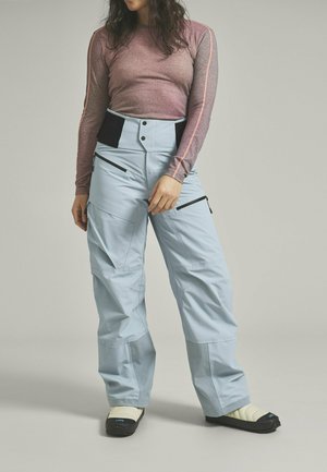Himmelblau Schnee trousers mit mehreren Reißverschlusstaschen und einem hohen Taillenbund. Kombiniert mit einem engen langärmeligen Shirt in Mauve mit pinken Akzenten.