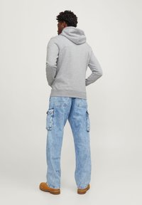 Sudadera gris con capucha y bolsillo frontal, combinada con pantalones cargo azul claro que tienen bolsillos laterales y zapatos marrones.