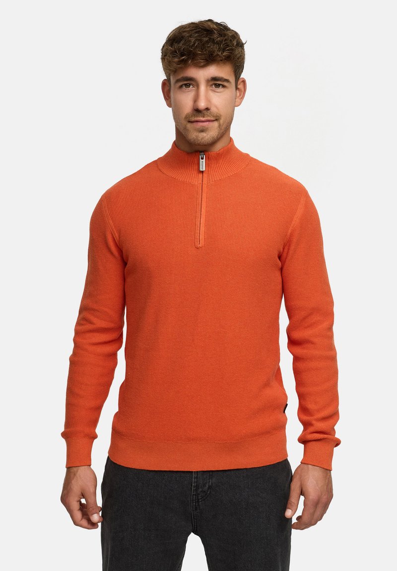 Orange langærmet sweater med høj krave og kvart lynlås. Lavet af strukturstrik materiale. Sammen med mørke jeans.