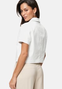 Korte witte linnen blouse met korte mouwen, een puntige kraag en een schone rugontwerp. Gedragen met lichtbeige hoge taillebroek.