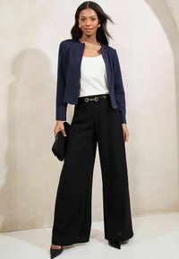Námořnická zkrácená bunda, bílý top, černé volné kalhoty s opaskem se zlatým akcentem. Černá spojka. Hladká tkanina, tailored design s uvolněným střihem.