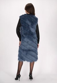 Lång blå faux fur-väst med ett lagerdesign som har texturerade ränder. Bärs över en svart långärmad topp och kombineras med svarta klackar.