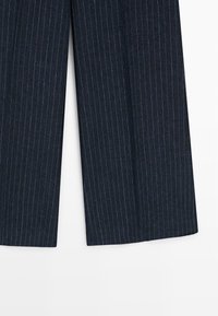 Pantalon large bleu marine à fines rayures blanches verticales, descendant jusqu’au sol.