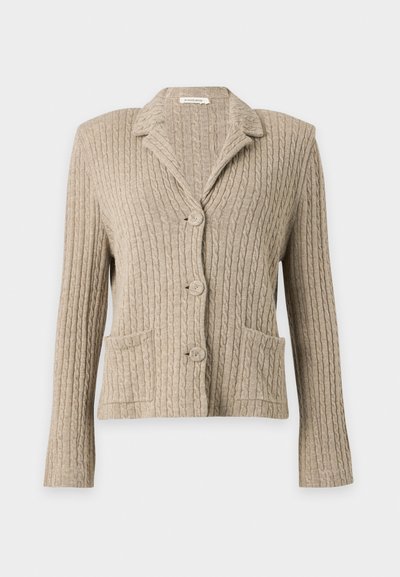 Cardigan beige en maille torsadée avec trois boutons, manches longues, col et deux poches avant, présenté sur un fond uni.