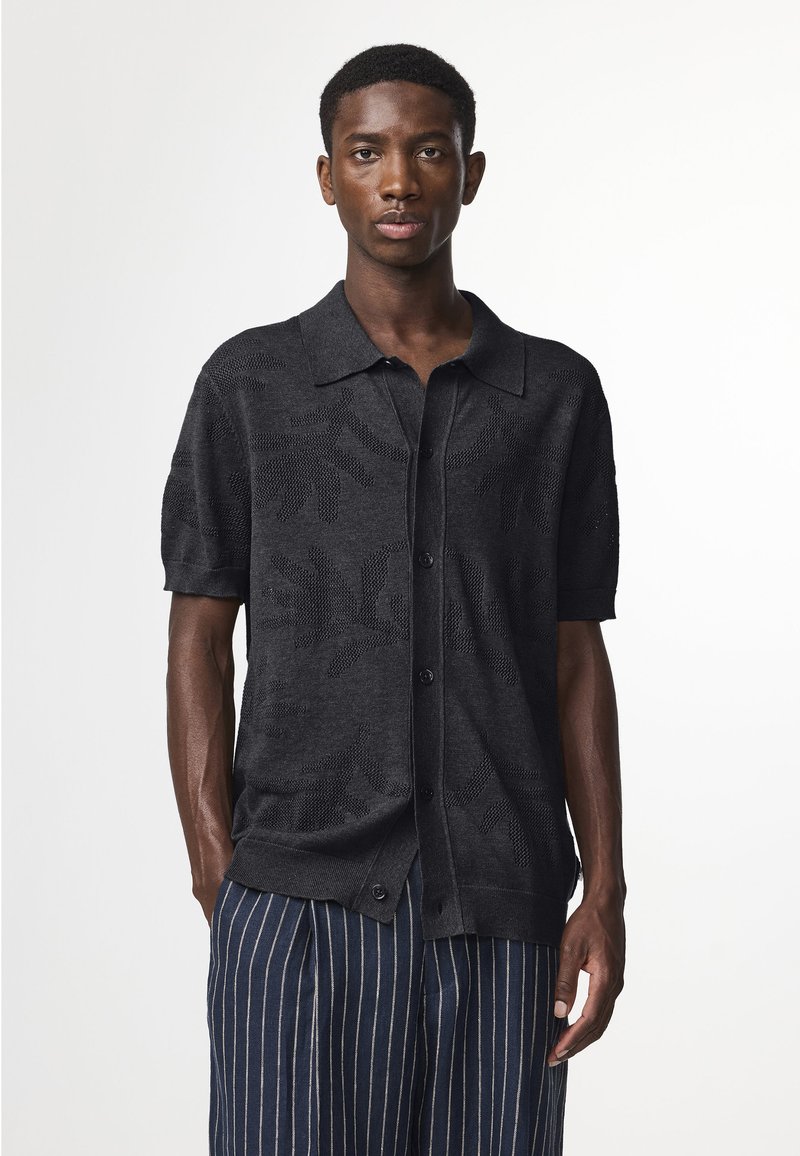 Zwarte kortefris knit shirt met een textuur van loofpatroon, knoopsluiting aan de voorkant en een klassieke kraag. Gekomt met blauw gestreepte broek.