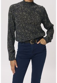 Bluzka z długim rękawem i wysokim kołnierzem, wykonana z ciemnogranatowej tkaniny zdobionej liściastym, kwiatowym wzorem w zielonych i niebieskich odcieniach.