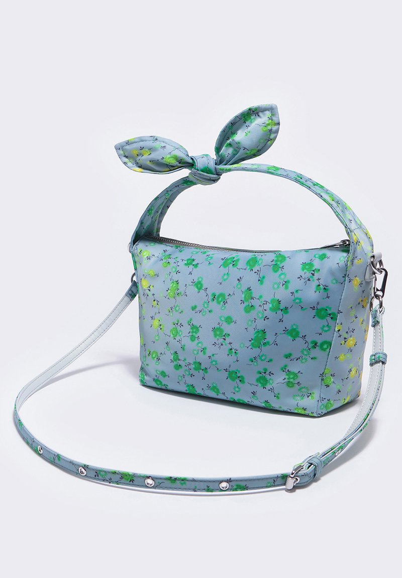 Bolso de tela azul claro con estampado floral en verde y amarillo. Presenta un detalle de nudo en el asa y una correa desmontable.