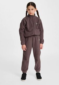 Tweedelig trainingspak in donker mauve stof met een jas met ritssluiting en broeken met elastische taille. Voorzien van een klein hartlogo en geribbelde manchetten.