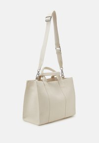 Vit canvasväska med dubbla handtag, justerbar axelrem och subtila stickningsdetaljer. Rektangulär form, slitstarkt material.