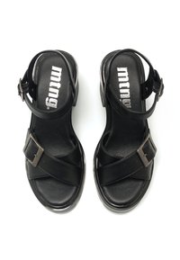 Sandalias negras con un diseño de tiras cruzadas, correa ajustable en el tobillo y un acento de hebilla metálica. Textura de cuero suave y plantilla acolchada.