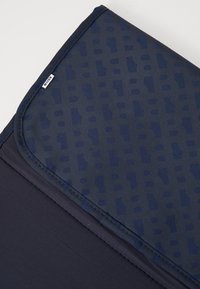 Mørkeblå stofflaptopdeksel med teksturert mønster, med en glatt overflate, kontraststing og et merketikett.