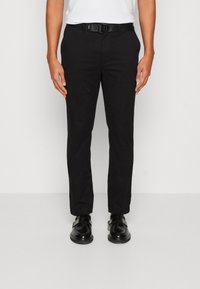 Pantaloni di cotone neri con una vestibilità slim, tasche frontali, passanti per cintura e una texture liscia. Abbinati a scarpe nere.