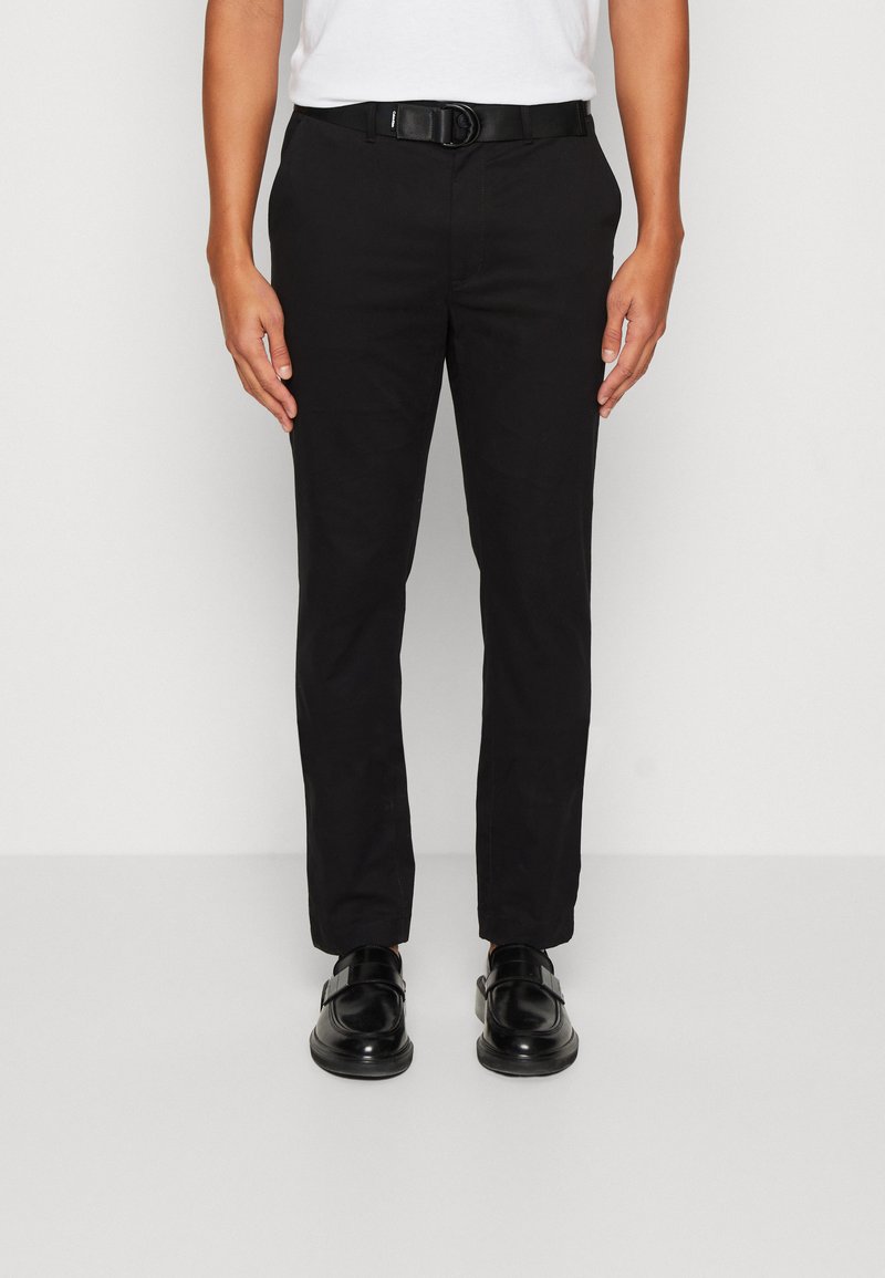 Pantaloni di cotone neri con una vestibilità slim, tasche frontali, passanti per cintura e una texture liscia. Abbinati a scarpe nere.
