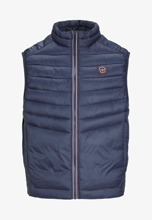 Tumedas sinine puffer vest, millel on kõrge kaelus, lukuga sulg ja horisontaalne tikandikujundus. Omab logot ja kahte küljetaskut.