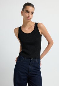 Top sin mangas de punto negro, con escote redondo. Combinado con jeans de mezclilla oscuros de talle alto. Textura suave, diseño ajustado.