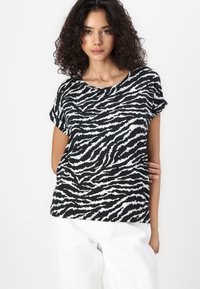 Svart og hvit zebra-stripete t-skjorte med kort erm og rund hals, laget av mykt stoff. Modellen har på seg hvite bukser, med avslappede armer.