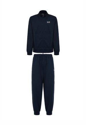 Completo tuta navy con giacca zip-up con colletto alto e polsini elasticizzati, abbinato a pantaloni con vita elasticizzata. Il tessuto sembra morbido.