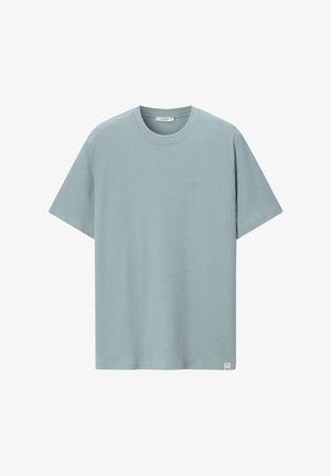 Hellblaues T-Shirt mit kurzen Ärmeln und Rundhalsausschnitt, mit kleinem gesticktem Logo auf der linken Brustpartie und einem Stofflabel nahe dem Saum.