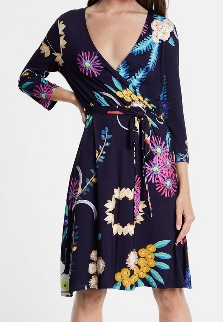 Femme portant une robe portefeuille bleu foncé à motif floral, manches trois-quarts et ceinture nouée à la taille.