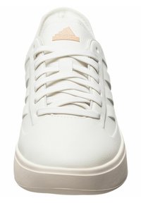 Sneaker bianca con finitura in pelle testurizzata, lacci bianchi piatti e logo Adidas color pesca chiaro. Punta arrotondata e design minimalista.