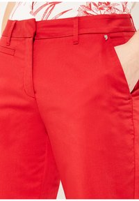 Pantalons rouges en tissu lisse, coupe ajustée, poches avant élégantes et un subtil accent métallique près de la taille.