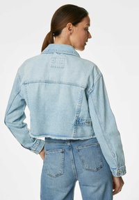 Giubbotto in denim azzurro chiaro con design corto, maniche lunghe e bordi sfilacciati. Presenta un colletto e dettagli con tasche posteriori.
