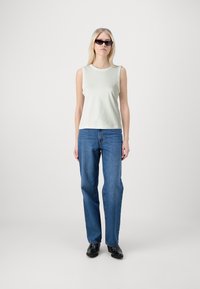Top sin mangas de color verde claro, tejido de peso medio; combinado con jeans rectos azules y zapatos negros; el modelo lleva gafas de sol negras y estrechas.