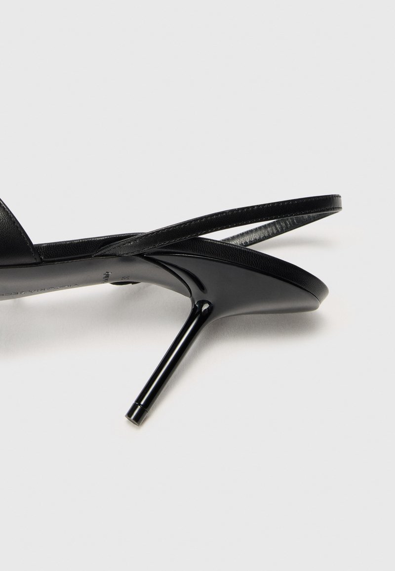 Des sandales à talons hauts noires présentent une finition en cuir brillant et lisse, des fines lanières et un bout pointu. Le talon mince accentue le design élégant.