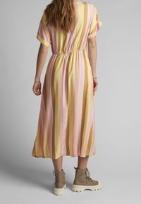 Robe midi à multiples rayures en rose pastel et jaune, avec manches courtes, taille élastique et tissu doux. Associée à des bottines à lacets neutres.