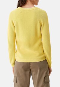 Gelber Strickpullover mit langen Ärmeln, gerippter Textur und rundem Ausschnitt. Abgebildet an einer Person, die khakifarbene Cargo-Hosen trägt.