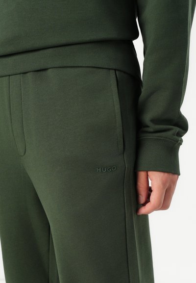 Jogging vert de Hugo avec ceinture côtelée, poches latérales et un logo subtil sur la cuisse. Tissu lisse avec une finition mate.
