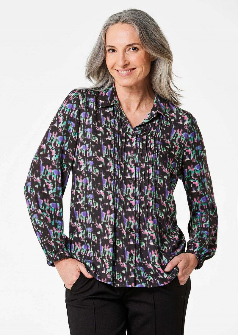 Blusa nera con motivo astratto multicolore, dotata di chiusura anteriore con bottoni, maniche lunghe e dettagli plissettati. Texture setosa.