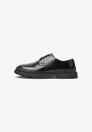 Sapato preto de couro com atacadores, solado de borracha espesso e costura detalhada, apresentado do lado externo sobre um fundo branco.