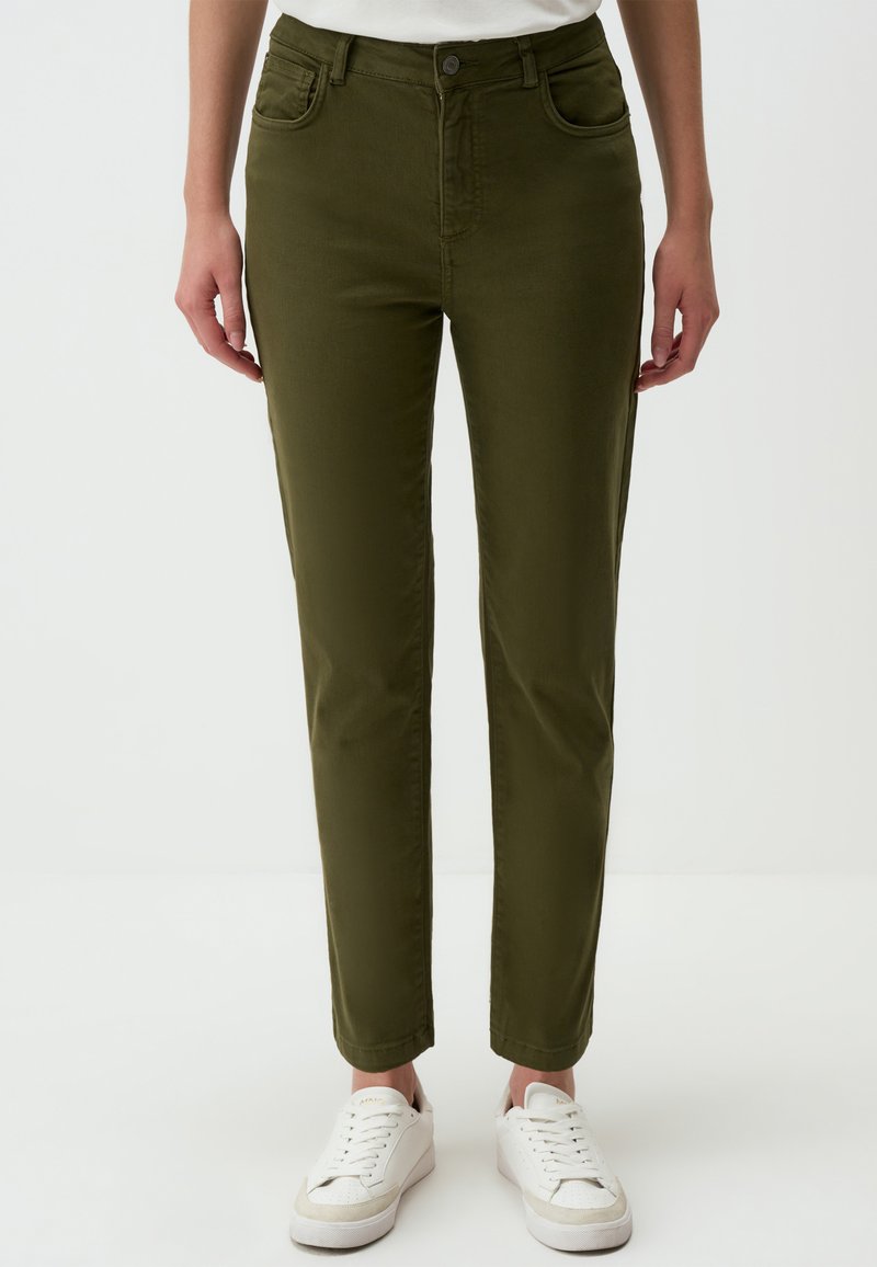 Olivengroene, slim-fit broek van zachte stof met vijf zakken, een knoopsluiting en een gladde textuur, gecombineerd met witte sneakers.