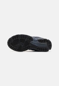 Black athletic shoe sole with a textured rubber surface featuring lug patterns for traction and a curved side profile for stability.