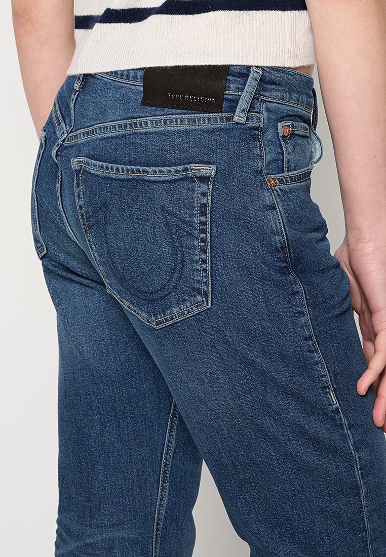 Dunkelblaue Denim-Jeans mit leichtem Stretch, Fünf-Taschen-Design und einem sichtbaren Logo-Patch am hinteren Bund. Auffällige Steppnähte.