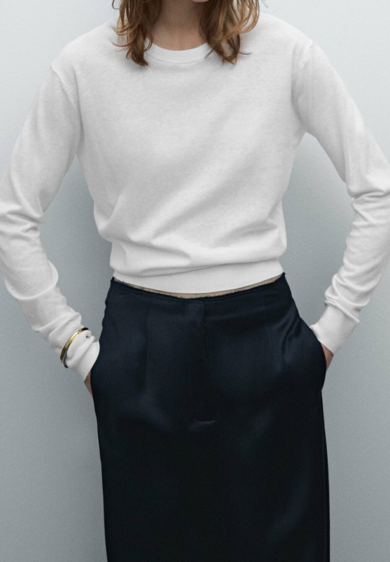 Vit långärmad sweatshirt med rund halsringning, kombinerad med navyblå satinsbyxor. Den släta texturen och den avslappnade passformen är framträdande egenskaper.