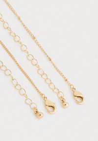 Zlaté tónované kovové reťazce s rôznymi veľkosťami článkov, obsahujúce zapínanie a guličkový akcent. Hladký povrch s lesklým finišom. Rôzne dĺžky.