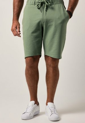 Grüne Shorts mit Waffelstruktur verfügen über einen Kordelzugbund, Seitentaschen und eine lockere Passform. Kombiniert mit weißen Sport Sneakers.