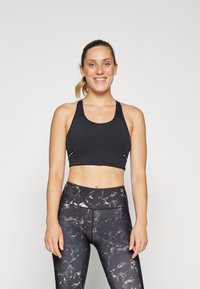Sort sports-bh med tynne stropper og sideglidelås, kombinert med høyde leggings med et marmorert svart og hvitt mønster.
