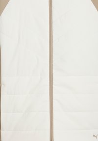 Padded vest in white and beige with a zip front, featuring diagonal quilted patterns and a small logo accent near the hem.