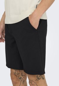 Sorte bomulds shorts med sidelommer, skræddertilpasset pasform og en ren kantfinish. Bæres med en beige top, der fremhæver et enkelt design.