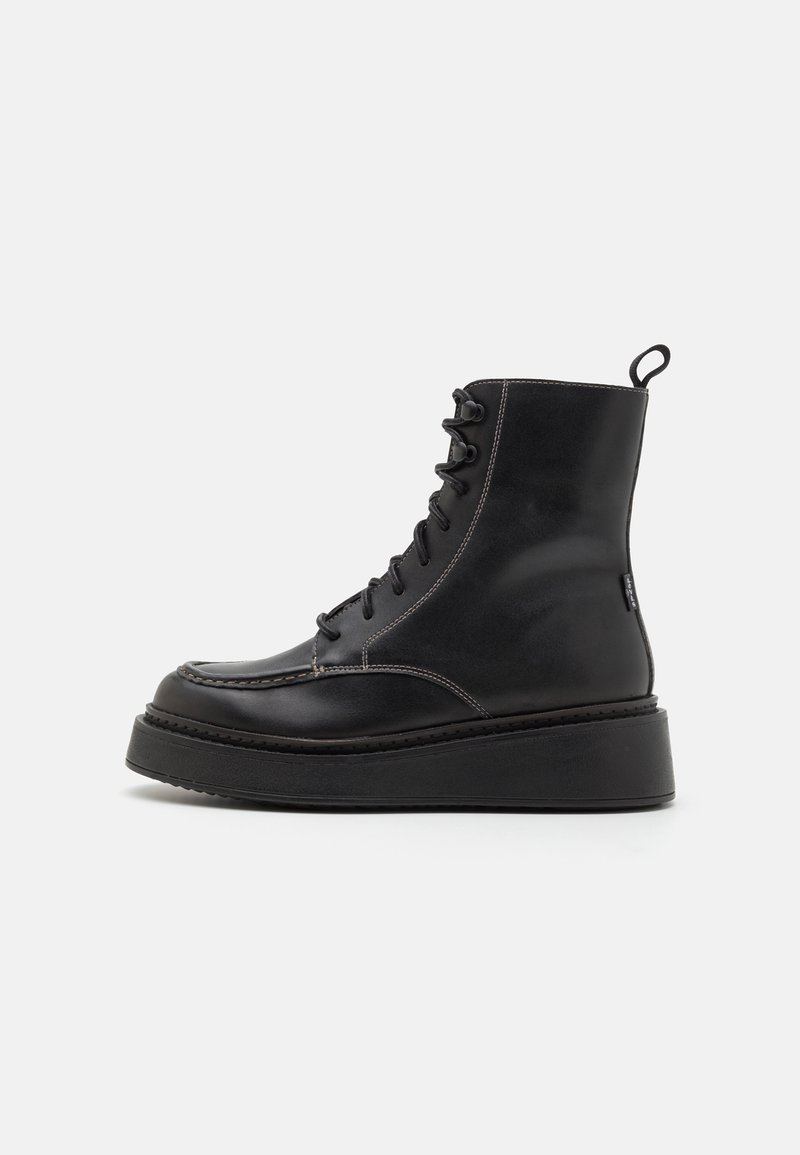 Botas de tornozelo em couro preto, com bico redondo, sola de plataforma espessa e sistema de atacadores. Apresenta costura em contraste e uma alça na parte de trás.