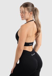 Zwarte sport-bh en leggings, gemaakt van rekbaar materiaal. De bh heeft een halternek en een open rugontwerp; de leggings hebben een hoge tailleband en logo-detail.