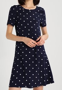 Námořnické modré šaty s krátkým rukávem a bílými puntíky, s kulatým výstřihem a volně střiženou sukní, která se jemně rozšiřuje.